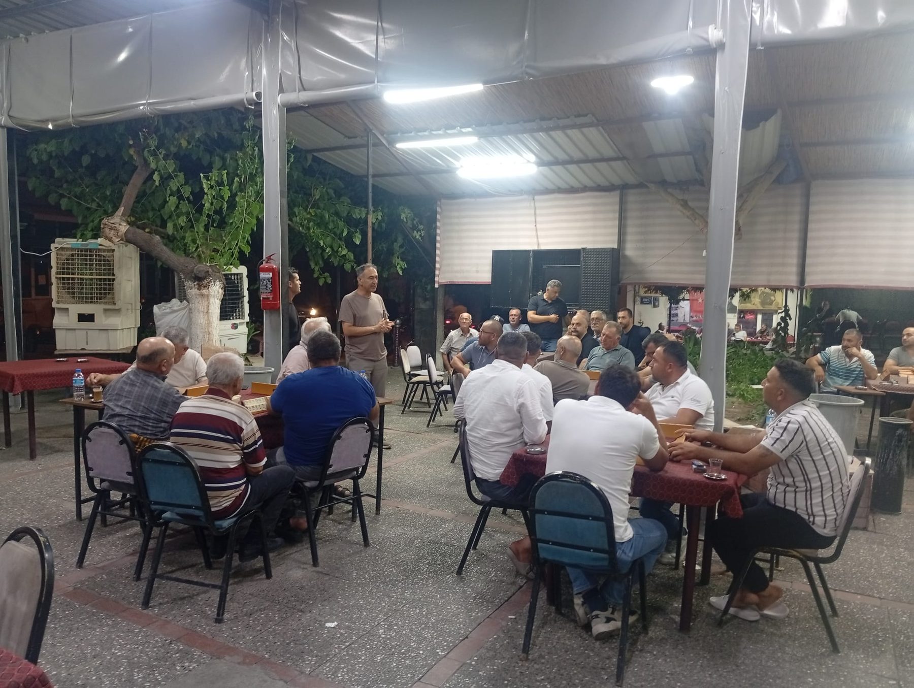 Açık bir toplantı alanında masalar çevresinde bir araya gelen mahalle sakinleri