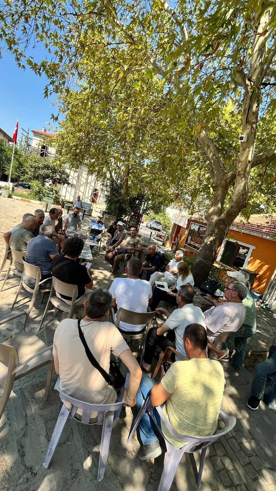 Köy meydanında ağaç gölgesinde oturarak konuşmayı dinleyen mahalle sakinleri