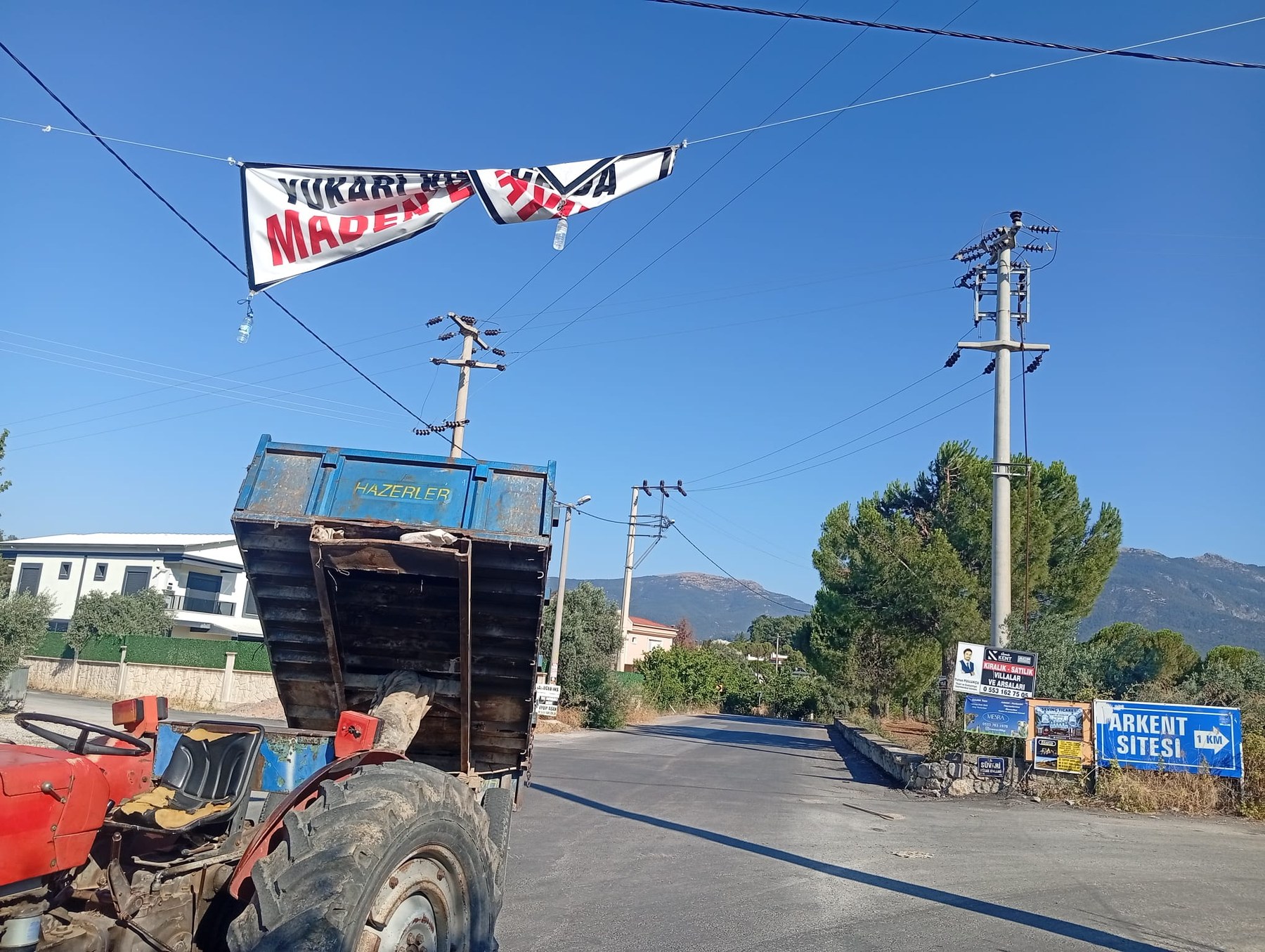 Madene Hayır pankartının altından geçen traktör ve köy yolu